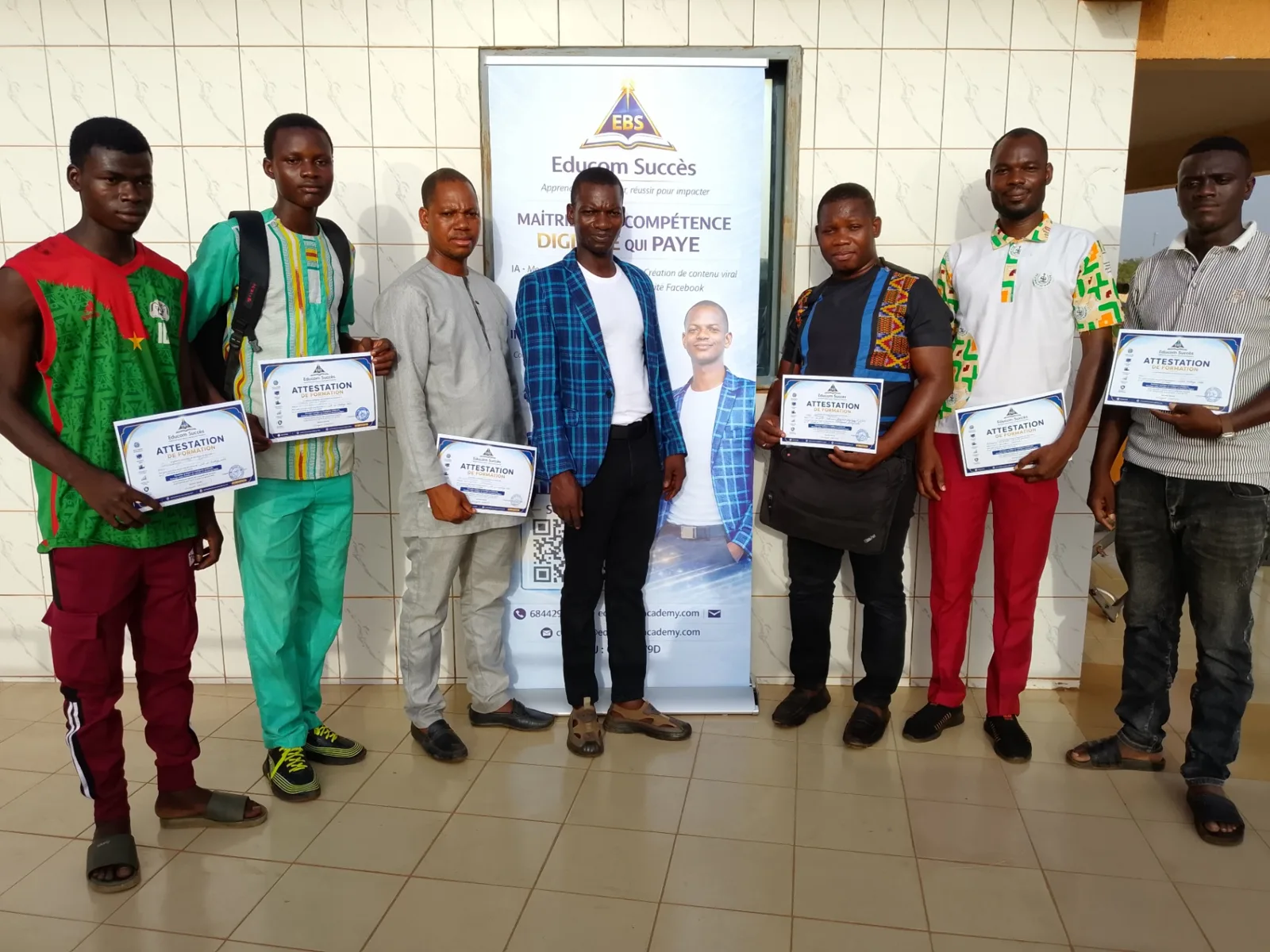 Groupe d’apprenants Educom Succès présentant leurs attestations de formation devant le kakémono
